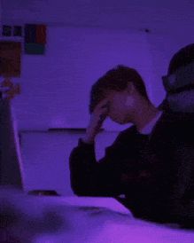 a man sitting in front of a laptop computer on top of a desk next to a purple light