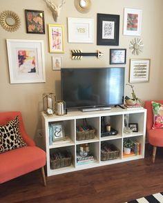 a television sitting on top of a white shelf next to two orange chairs and a black and white rug