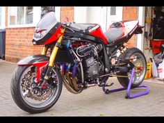 a red and black motorcycle parked in front of a brick building next to a purple pipe