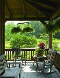 a porch with rocking chairs and potted plants on the back deck overlooking a wooded area