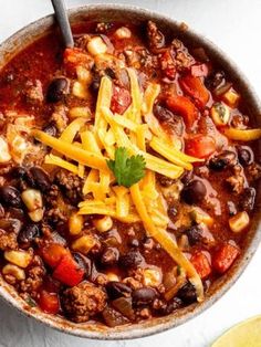 a bowl filled with chili and cheese on top of a white table next to a spoon