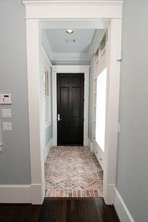 an empty hallway with wood floors and white trim on the walls, leading to a black door