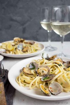 two plates of pasta with clams and wine glasses on the table next to them