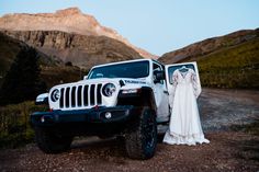 a bride and groom standing in front of a white jeep with mountains in the background