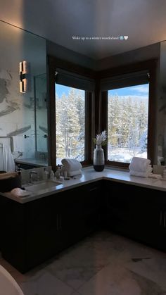 a large bathroom with two sinks and a tub in it's corner, looking out onto the snowy mountains