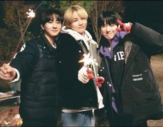 three young people standing next to each other near a fire pit with sparklers in their hands