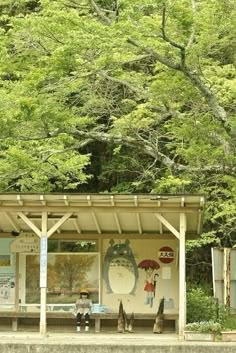 a woman sitting on a bench in front of a small building with trees behind her