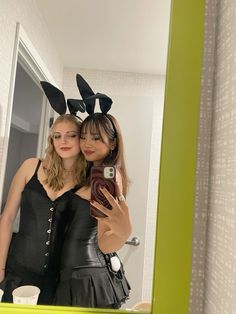 two women dressed up in bunny ears taking a selfie with their cell phone while standing in front of a mirror