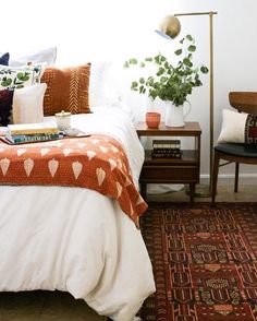 a bed with pillows and blankets on it next to a lamp, chair and table