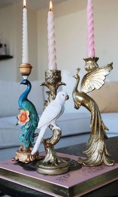 three candles are sitting on a table with two figurines and one is holding a bird