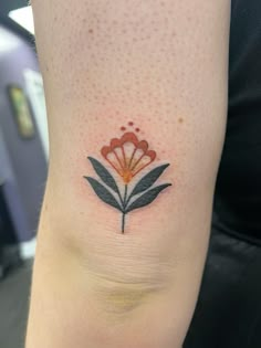 a small flower tattoo on the ankle is shown in red and orange colors with black leaves