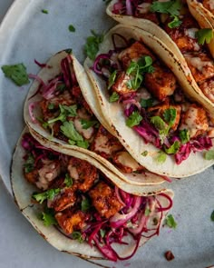 three tacos on a plate with shredded red cabbage