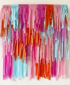 colorful streamers are hanging on the wall in front of a white wall with an orange, pink, and blue backdrop