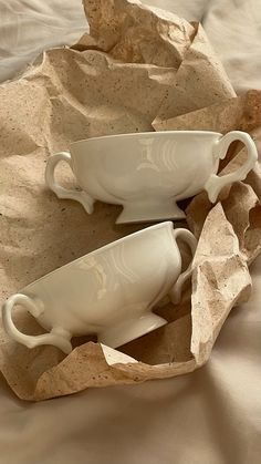 two white cups and saucers sitting on top of a table cloth covered bed sheet