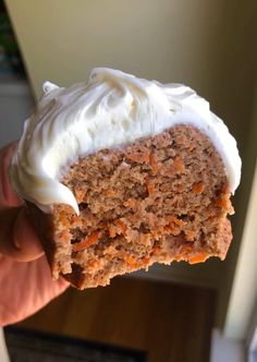 a person holding up a piece of carrot cake with cream cheese frosting on top