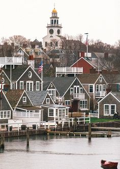 a row of houses on the water with a clock tower in the backgroud