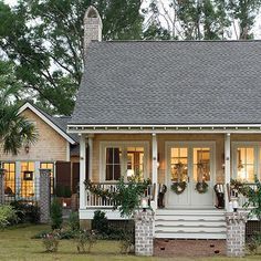 a small white house with porches and plants on the front door is surrounded by greenery