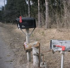 two mailboxes sitting on the side of a dirt road in front of trees