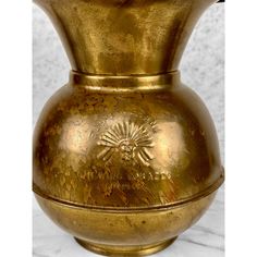 a gold colored vase sitting on top of a marble countertop next to a white wall