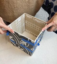 two hands are opening up a box with blue handles on a white tablecloth covered surface