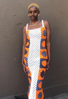 a woman standing in front of a wall wearing an orange and white crochet dress