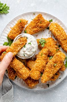 someone is dipping sauce on some fried chicken tenders with ranch dressing in a white bowl