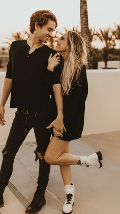 a man and woman standing next to each other on the sidewalk with palm trees in the background