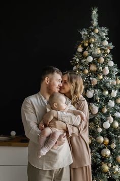 a man and woman holding a baby in front of a christmas tree