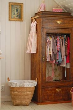 a wooden cabinet with clothes hanging on it's sides and a basket next to it