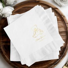 four white napkins with gold foil on them sitting on a wooden plate next to flowers