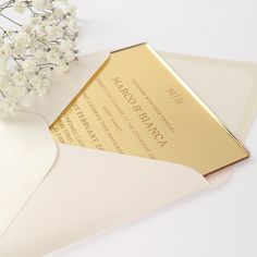 a white envelope with gold foil on it next to a bouquet of baby's breath flowers