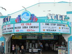 people are walking in front of a store with signs on the side of it that read, surf