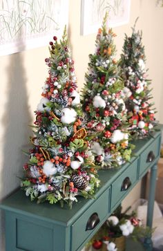 three small christmas trees on top of a green dresser