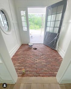 an open door leading into a room with brick flooring and white paint on the walls