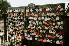 there are many mugs hanging on the side of this fence, which is decorated with tea cups