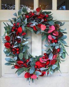 a wreath with red flowers and green leaves hanging on the front door to give it a festive feel