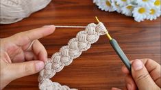 someone crocheting a piece of white yarn on a table with flowers in the background