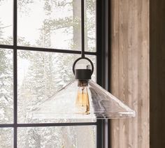 a glass light hanging from the side of a window in front of snow covered trees