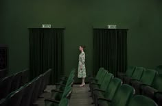 a woman standing in the middle of an empty auditorium filled with green chairs and black drapes