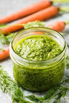 a jar filled with green pest next to carrots