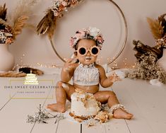 a baby sitting on the floor with a cake in front of her and wearing sunglasses