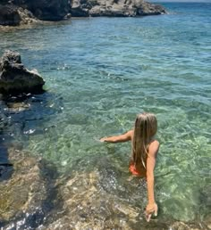 a woman wading in the water near rocks