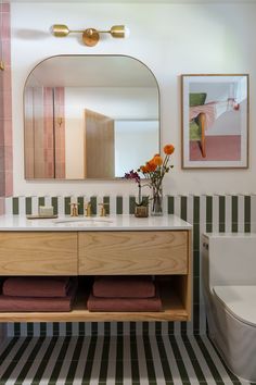 a bathroom with a sink, mirror, toilet and flowers in vases on the counter