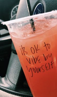 a drink in a plastic cup sitting on top of a car steering wheel with the words it's ok to vibe by yourself