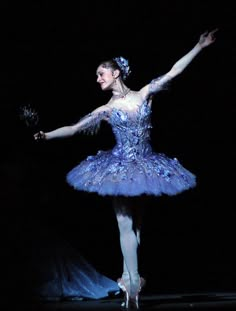 the ballerina is dressed in blue and holding her arms out to the side with one hand