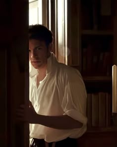 a man in white shirt standing next to a book shelf