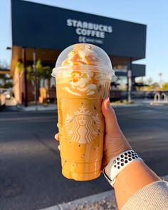 a person holding up a starbucks drink in front of a building