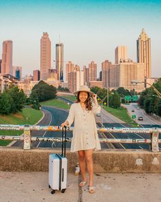 a woman standing on the side of a bridge with her suitcase and hat in hand