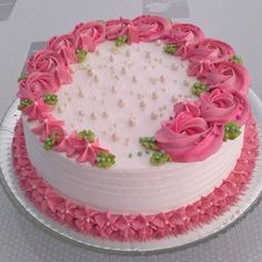 a white cake with pink frosting roses and pearls on the top is sitting on a plate