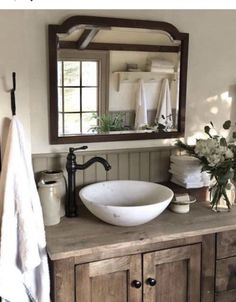 a bathroom sink sitting under a mirror next to a wooden cabinet and counter top in front of a window